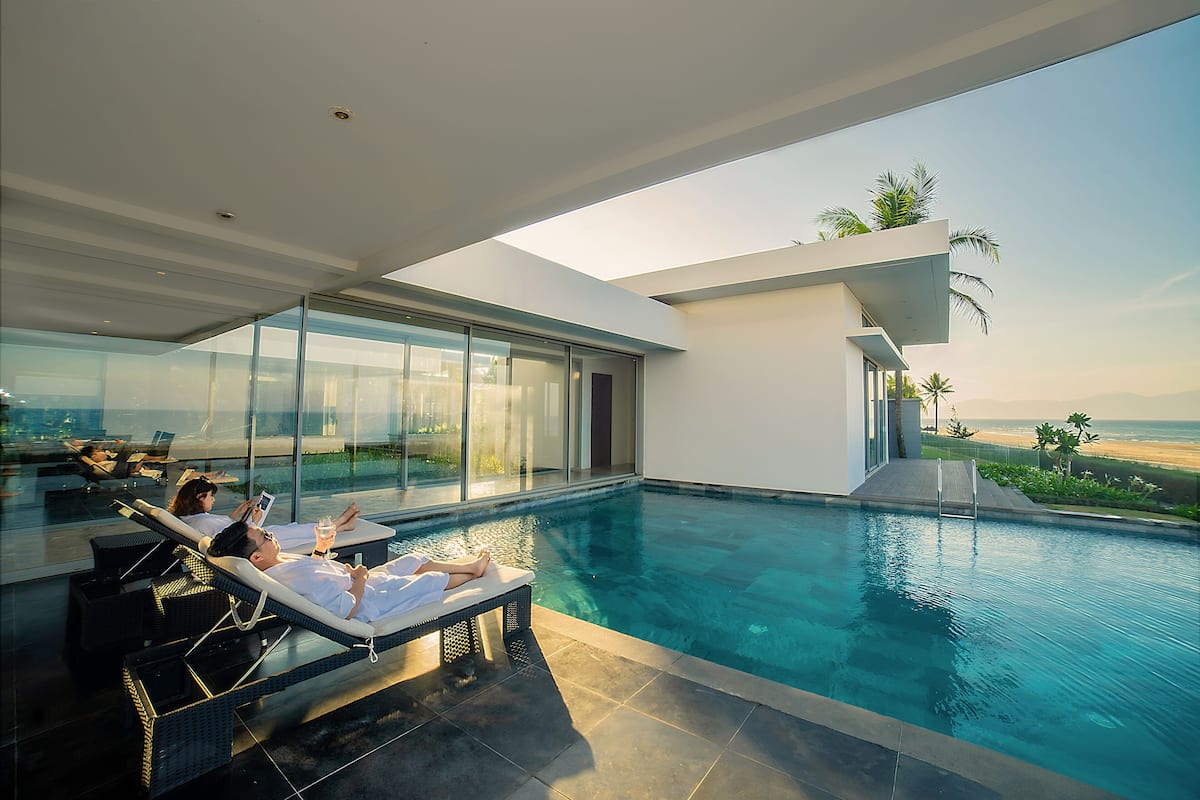 A modern infinity pool with clear views of the ocean, lounge chairs, and a glass-enclosed area.