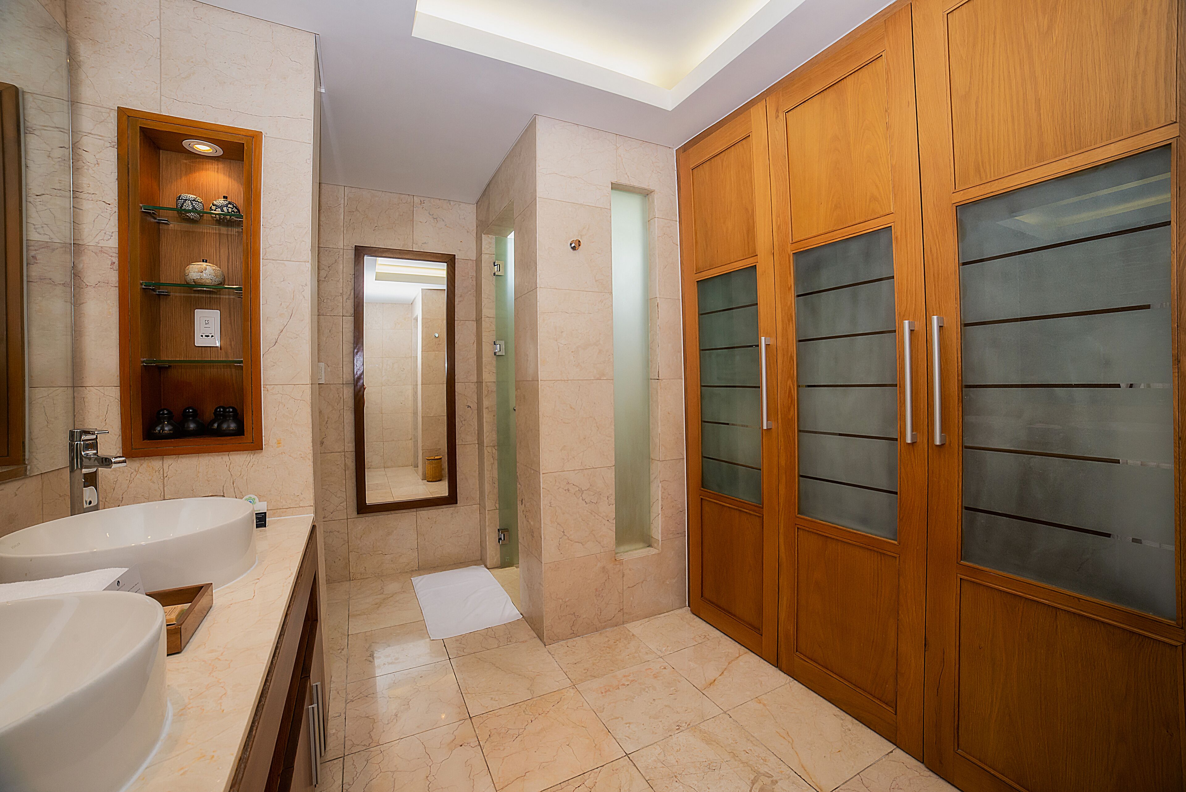 A modern bathroom with two sinks, a vanity, a mirror, and wooden cabinets with frosted glass doors.