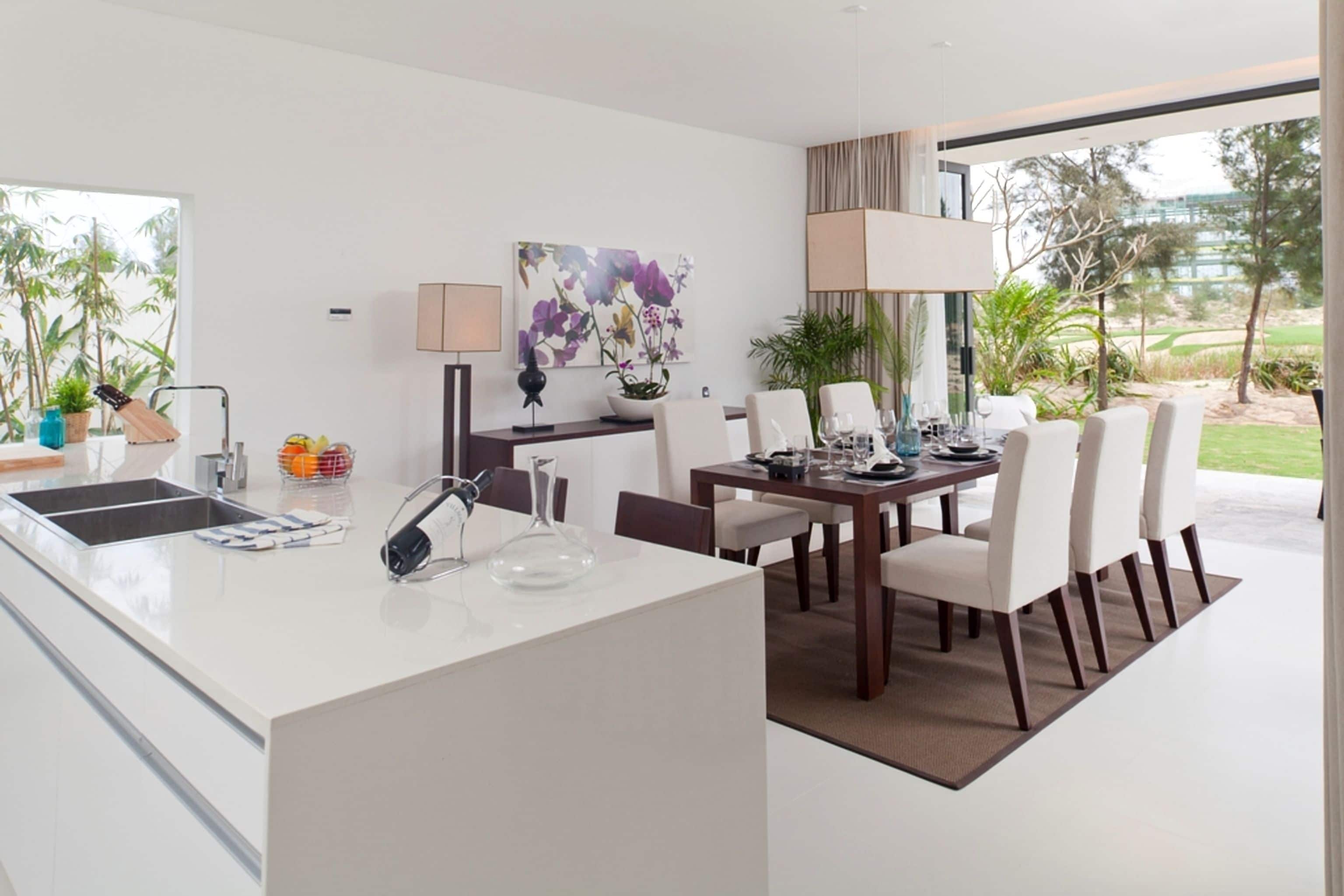 Eine moderne Küche mit weißer Arbeitsplatte, ein Essbereich mit Tisch und Stühlen sowie ein Blick ins Freie.
