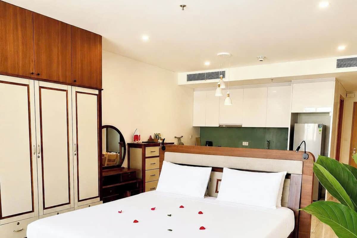 A bedroom with a wooden bed, a wardrobe, a desk, and a kitchenette.