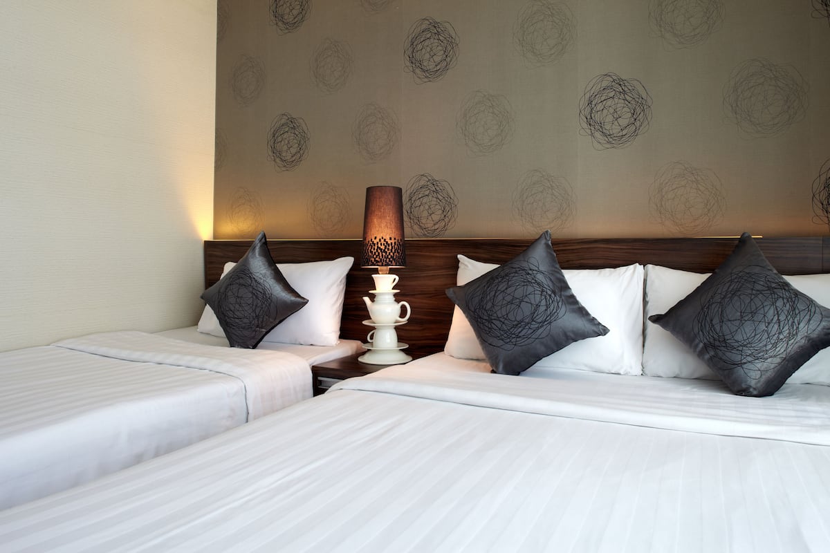 Ein Hotelzimmer mit zwei Betten, einem Nachttisch, einer Lampe und einem Wandpapier mit Muster.