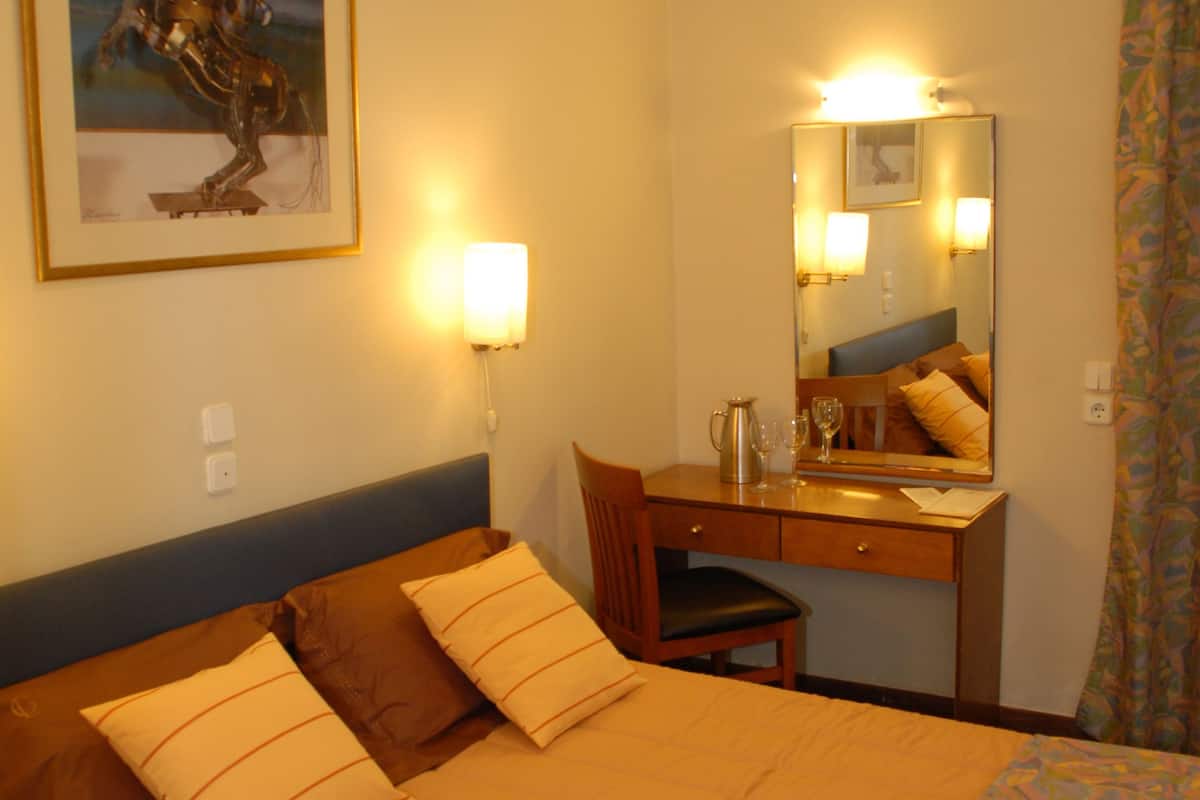 A hotel room with a bed, a desk, a chair, a mirror, and a painting on the wall.