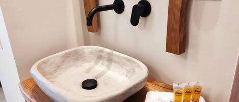 Un baño con un lavamanos grande de forma ovalada de piedra, encimera de madera y una bandeja pequeña con dispensadores de jabón.