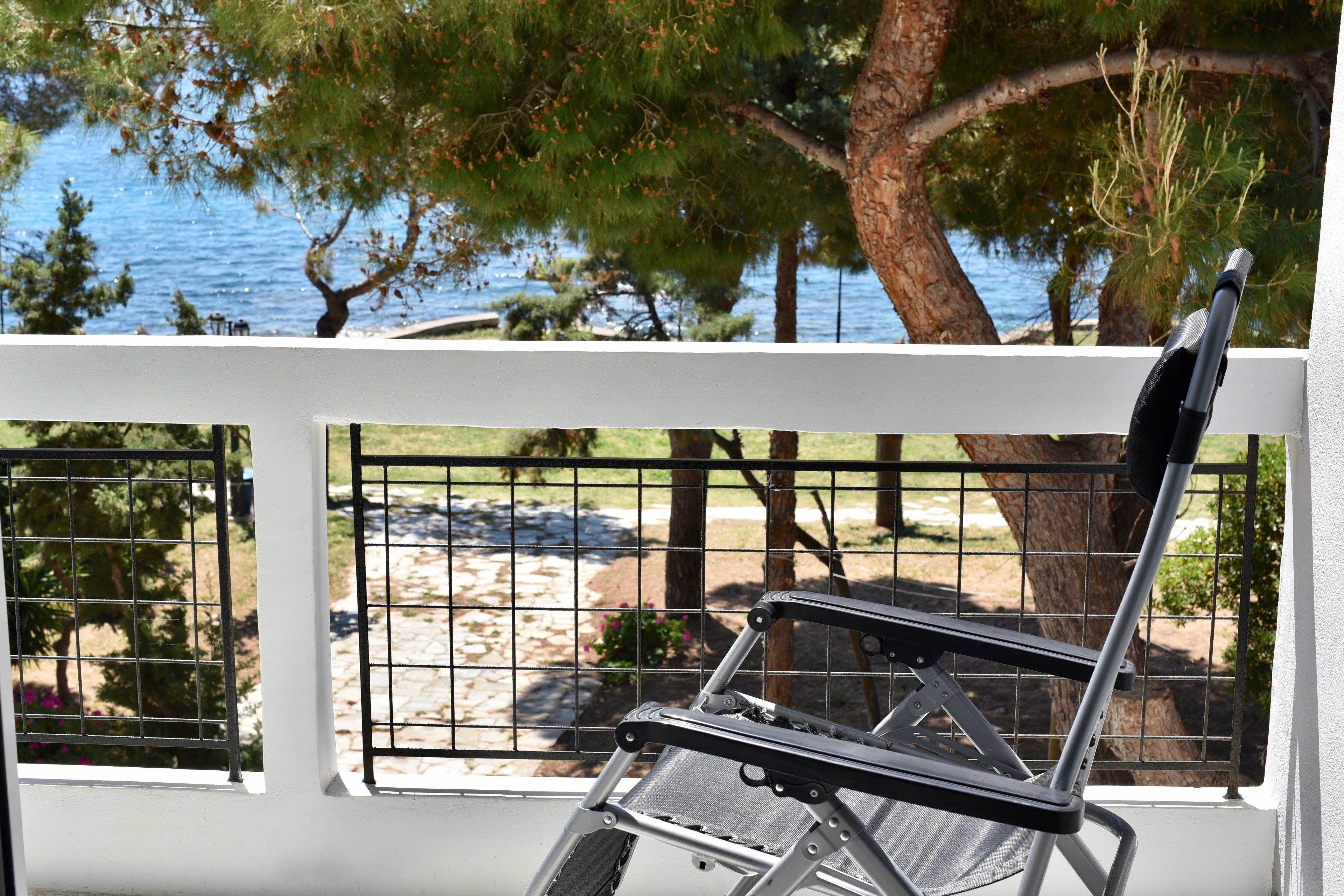 A white balcony with a metal railing overlooking a beach and trees.