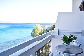 Ein Balkon mit freiem Blick auf das Meer, ein Glastisch mit einer Vase grüner Pflanzen und ein weißes Geländer.