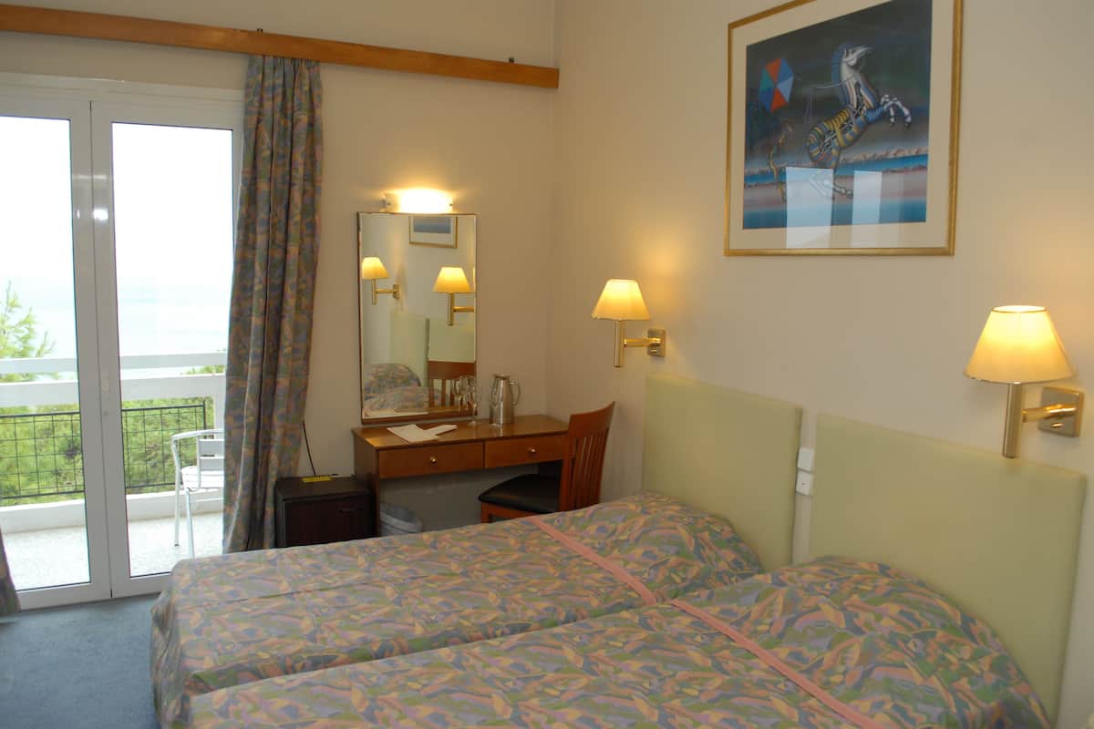 A hotel room with two beds, a desk, a chair, a window with curtains, a painting on the wall, and two wall lamps.
