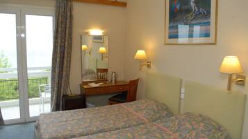 Une chambre d’hôtel avec deux lits, un bureau, une chaise, une fenêtre avec des rideaux, un tableau au mur et deux lampes murales.