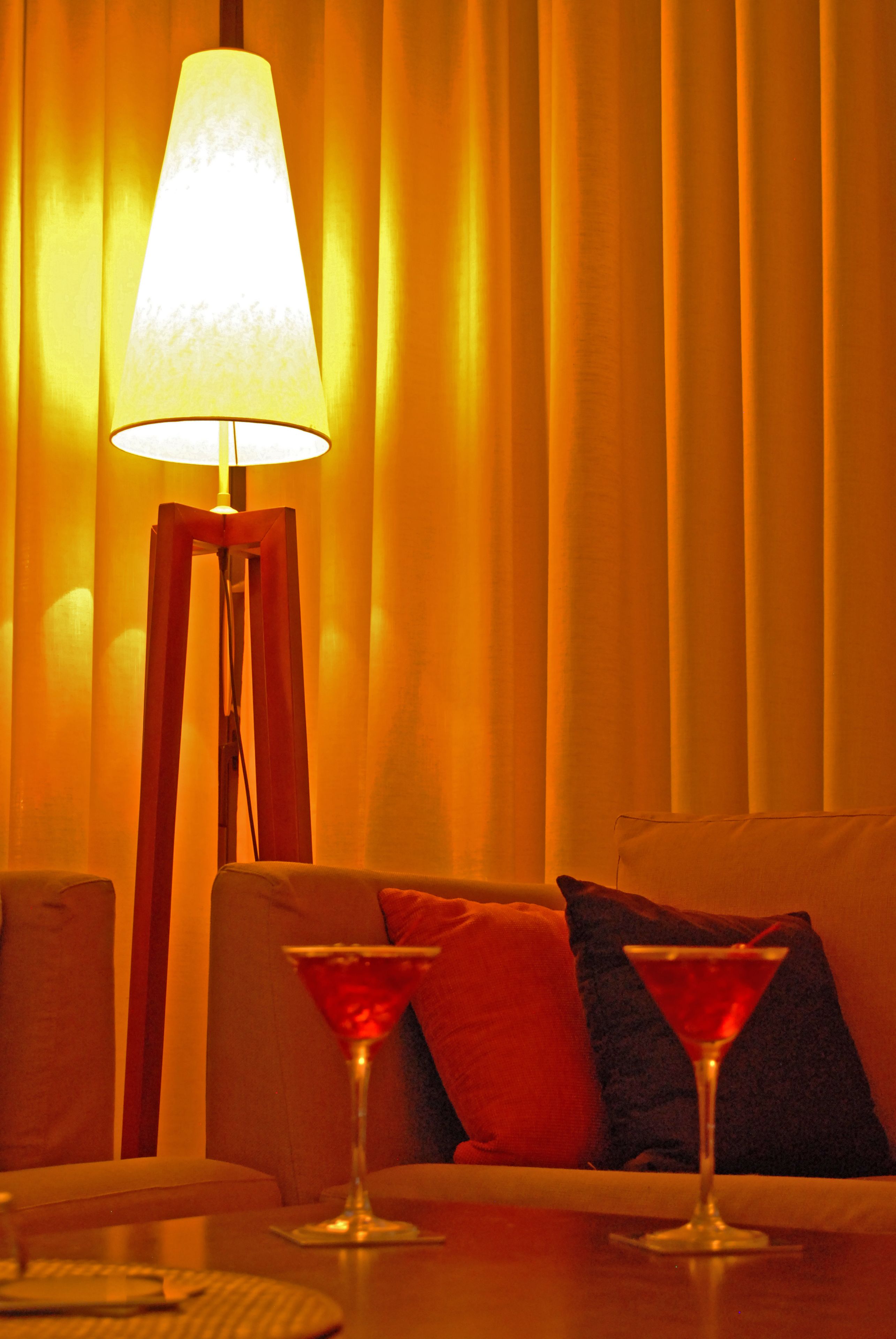 Une pièce avec un canapé, deux verres à cocktail rouges, une lampe sur pied et des rideaux.
