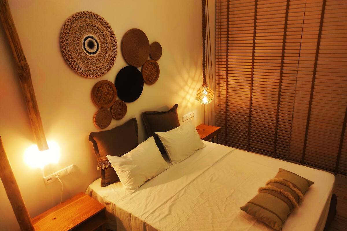 A neatly made bed with white linens and multiple pillows, a wooden headboard, and a bedside table with a lamp.