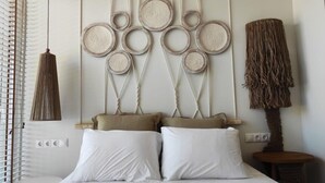 Un dormitorio con cama, almohadas blancas, un cabecero de macramé montado en la pared y una lámpara de fibras naturales.