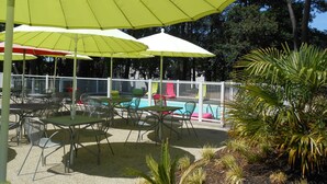 Terraza exterior con sombrillas, piscina y zona vallada con sillas.