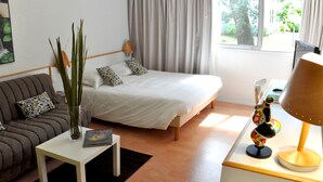 Una habitación de hotel con una cama, un sofá, una mesita con un jarrón y un libro, y una lámpara.