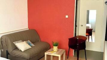 Una habitación pequeña y acogedora con una pared roja decorativa, un sofá, una mesita con una planta, una silla y una cama.