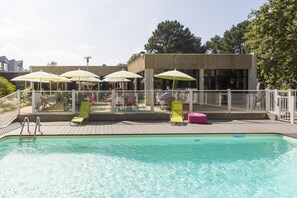 A swimming pool with lounge chairs and umbrellas, surrounded by a white fence and a building with large windows. - Lorient Résidence (Caudan)