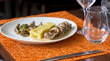 Un plato de comida con champiñones, puré de patatas y salchicha sobre un mantel individual naranja.