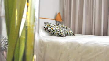 Et hotelværelse med en seng, en pude, en vase med grønne planter og en lampe.