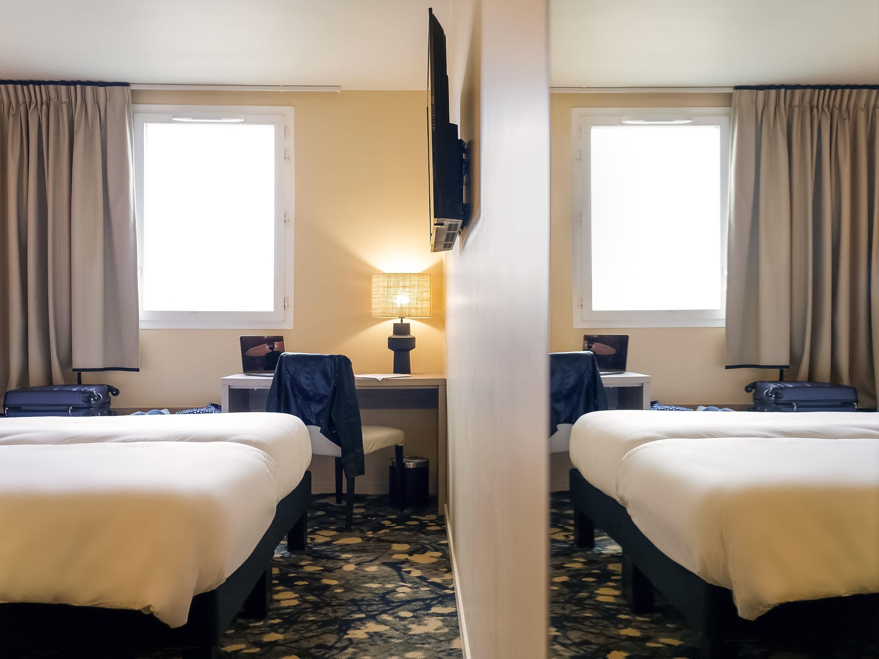 Een hotelkamer met twee bedden, een bureau met een laptop, een lamp en een televisie die aan de muur is bevestigd.