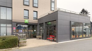 Een modern gebouw met een glazen gevel, een rode bank voor de deur en een kleine tuin.