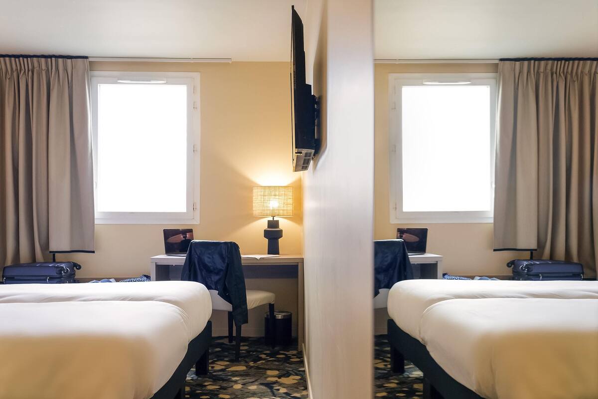 Een hotelkamer met twee bedden, een bureau met een laptop, een lamp en een televisie die aan de muur is bevestigd.