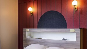 Een bed met een houten hoofdbord, twee wandlampen en een groot donker rond ontwerp daarboven.