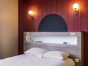 Una cama con cabecera de madera, dos lámparas fijadas a la pared y un diseño circular oscuro y grande sobre la cabecera.