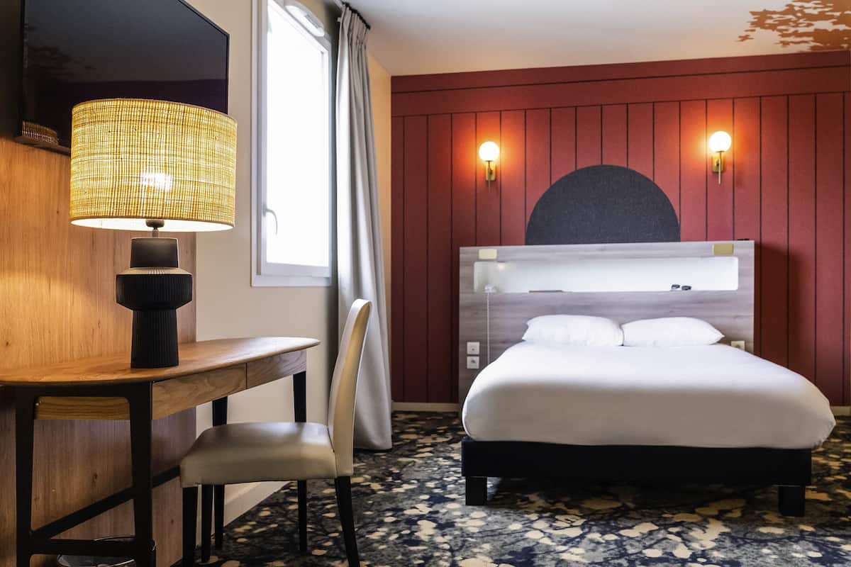 Een hotelkamer met een bed, een bureau, een stoel, een lamp en twee wandlampen.