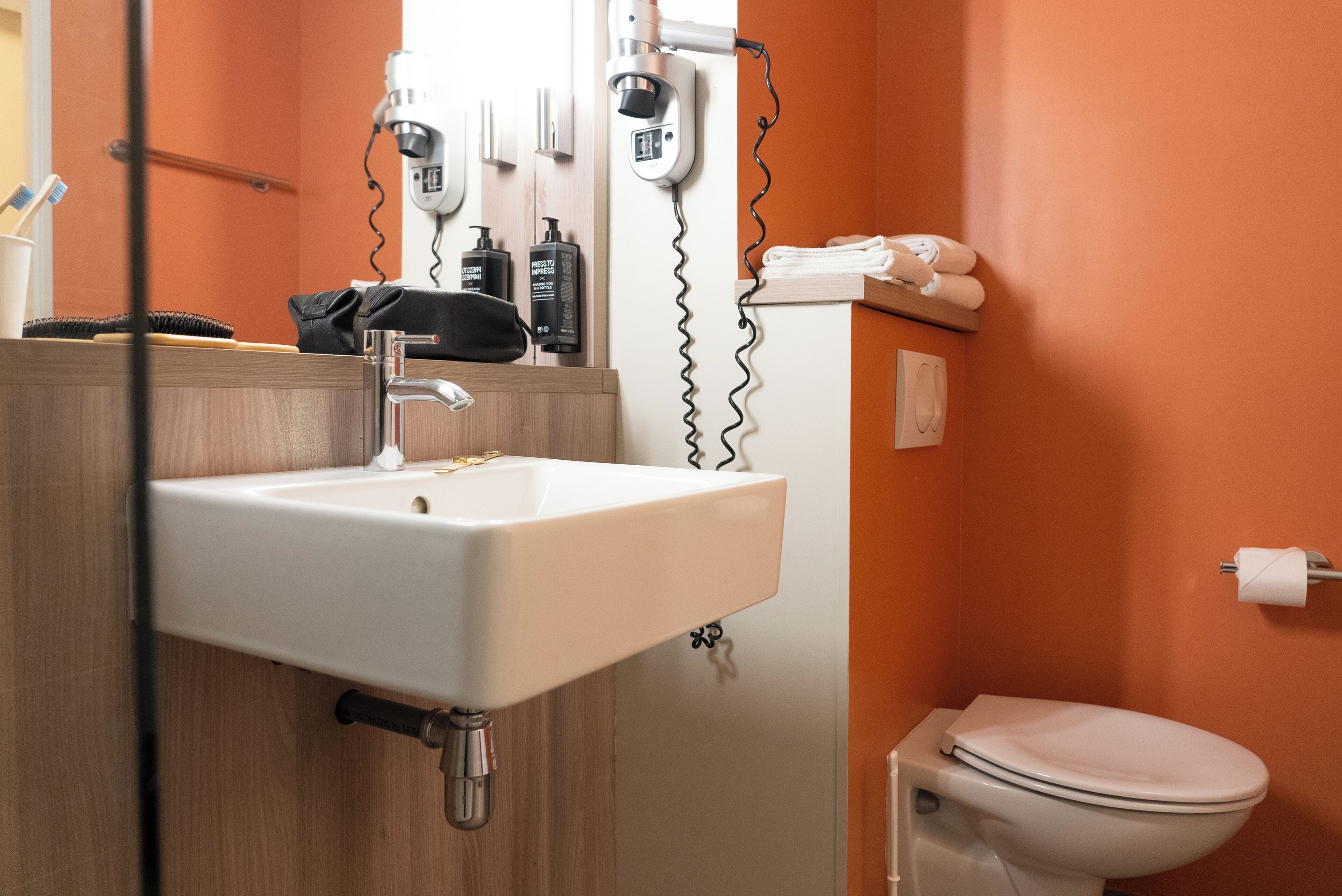 A bathroom with a white sink, a toilet, and a hairdryer mounted on the wall.