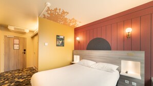 A hotel room with a large bed, a wooden headboard, two bedside lamps, and a wall-mounted light fixture.