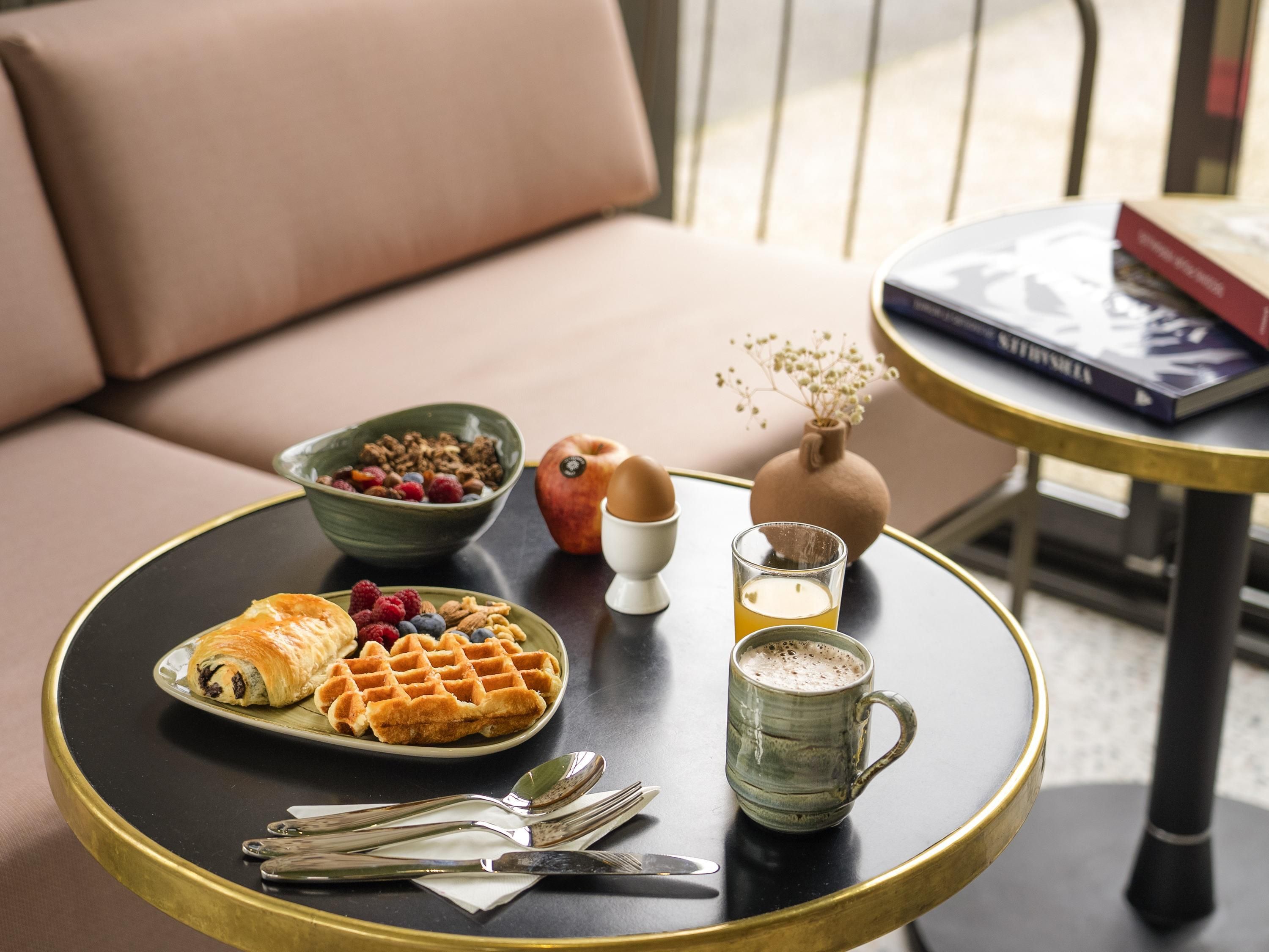Un plateau de petit-déjeuner avec des gaufres, des fruits rouges, un croissant et une tasse, posé sur une table ronde.
