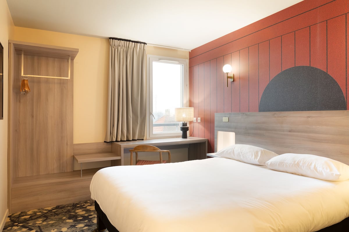 Een hotelkamer met een bed, een bureau, een stoel, een lamp en uitzicht.