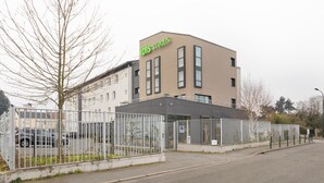 Een modern gebouw met een bord waarop “ibis styles” staat en een hekwerk.