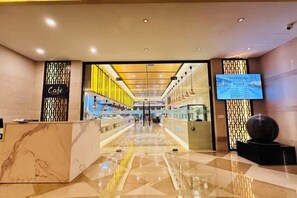 Un hall de hotel con mostrador de recepción, zona de cafetería y una gran pantalla digital.