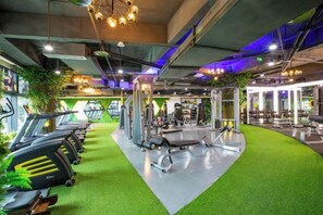 Un gimnasio con cintas de correr, pesas y suelo verde.