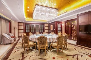 Comedor con una mesa redonda dispuesta para ocho personas, rodeada de sillas ornamentadas, un candelabro y una pantalla grande en la pared.