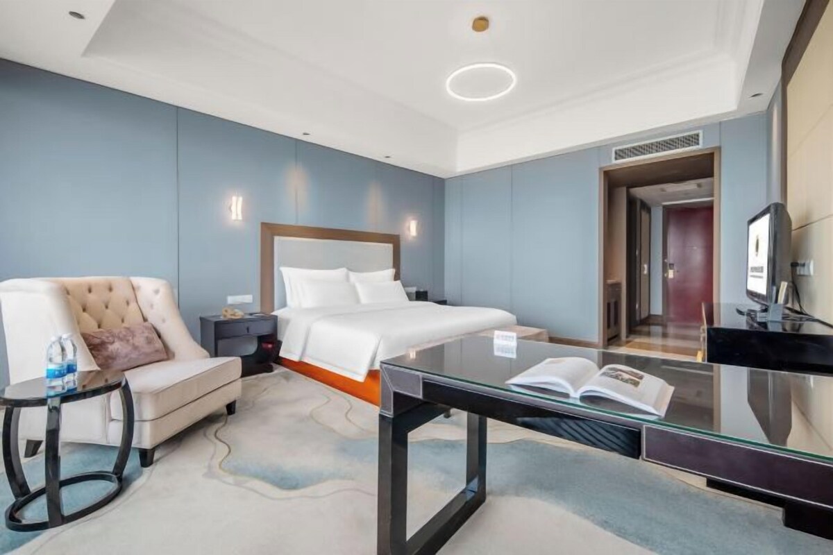 Habitación de hotel con cama, sofá, escritorio y un libro, y televisor.
