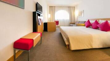 A hotel room with a bed, a desk, a TV, and a window with curtains.