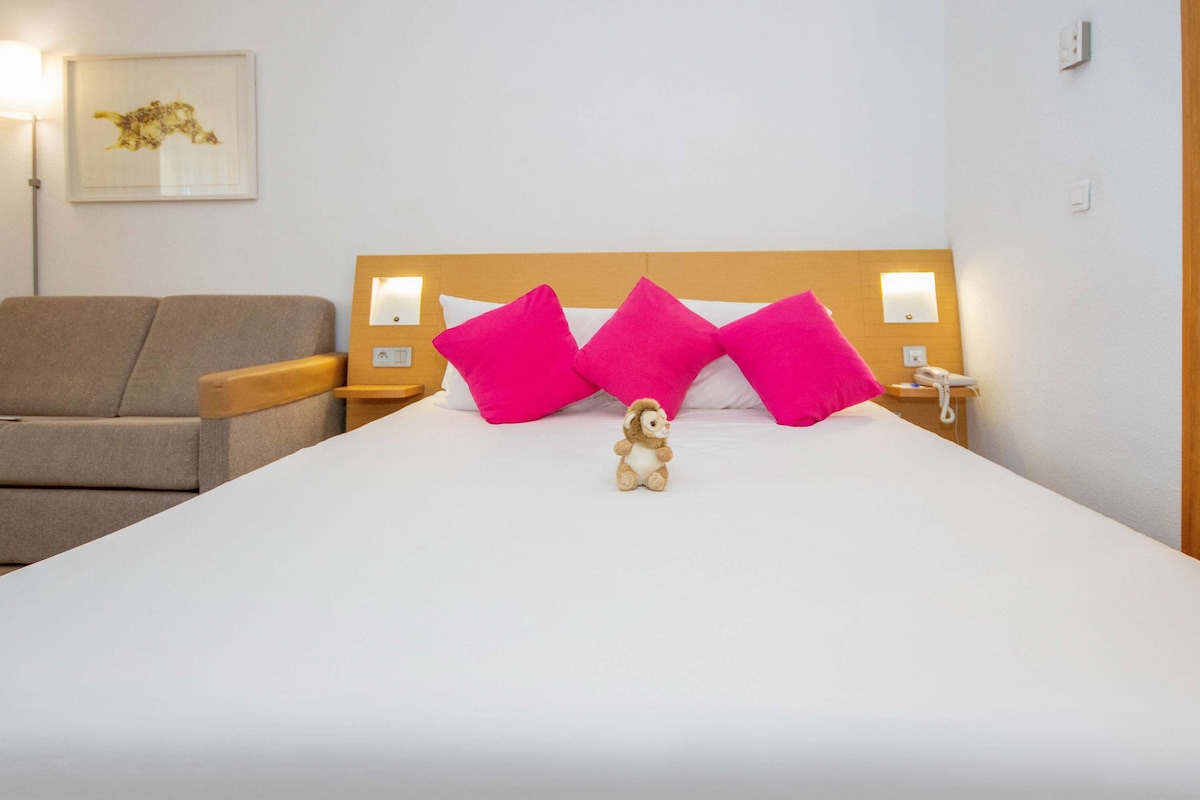 Una habitación de hotel con una cama grande, dos mesitas de noche, una lámpara, un sofá y un cuadro en la pared.