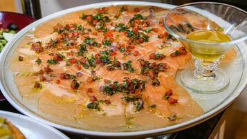 Un plato grande de salmón adornado con hierbas y tomates en cubos, acompañado de un vaso de aceite de oliva.