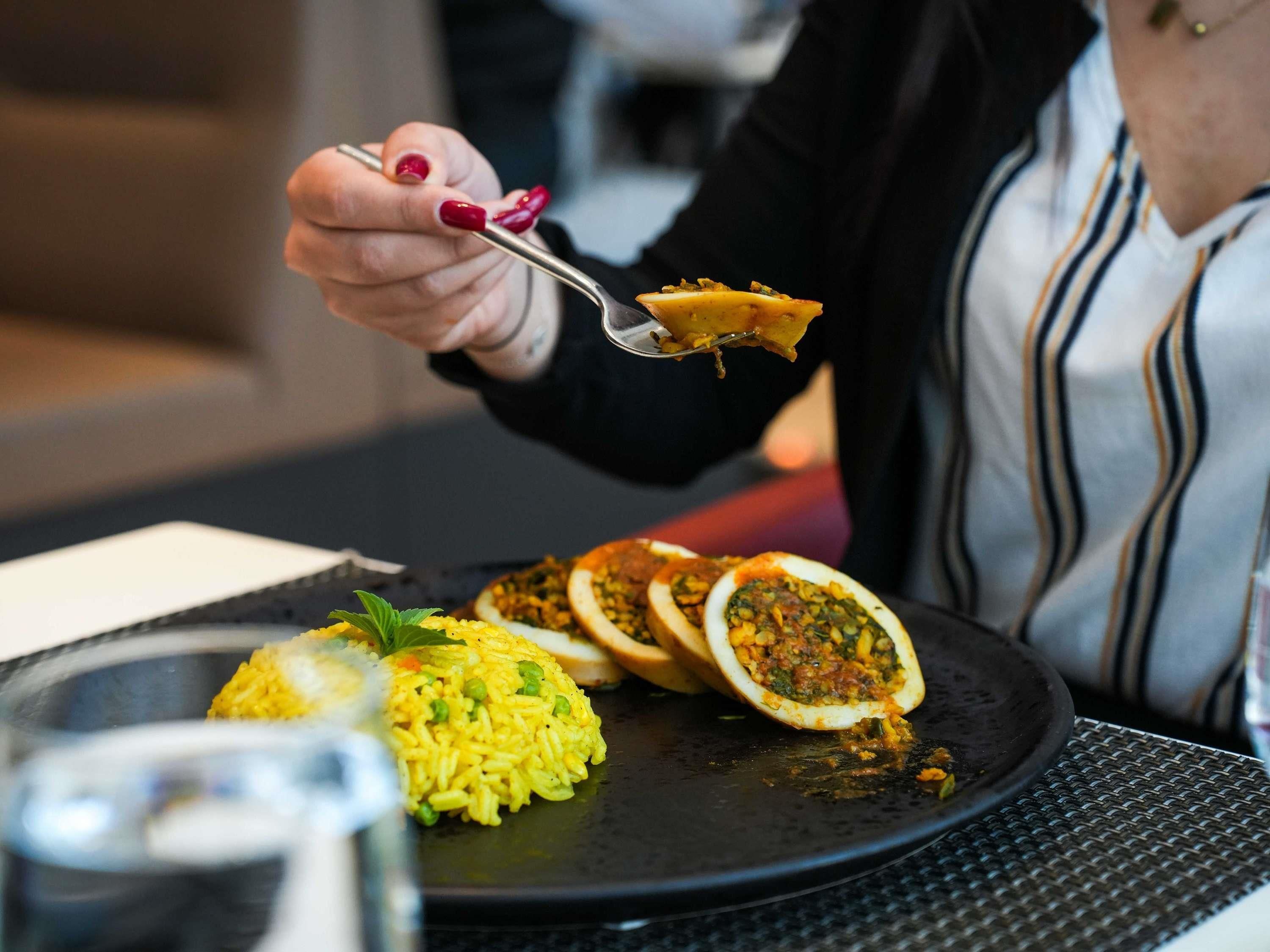 Una persona cenando en una mesa con un plato negro que contiene arroz amarillo, pimientos rellenos y un tazón de sopa.