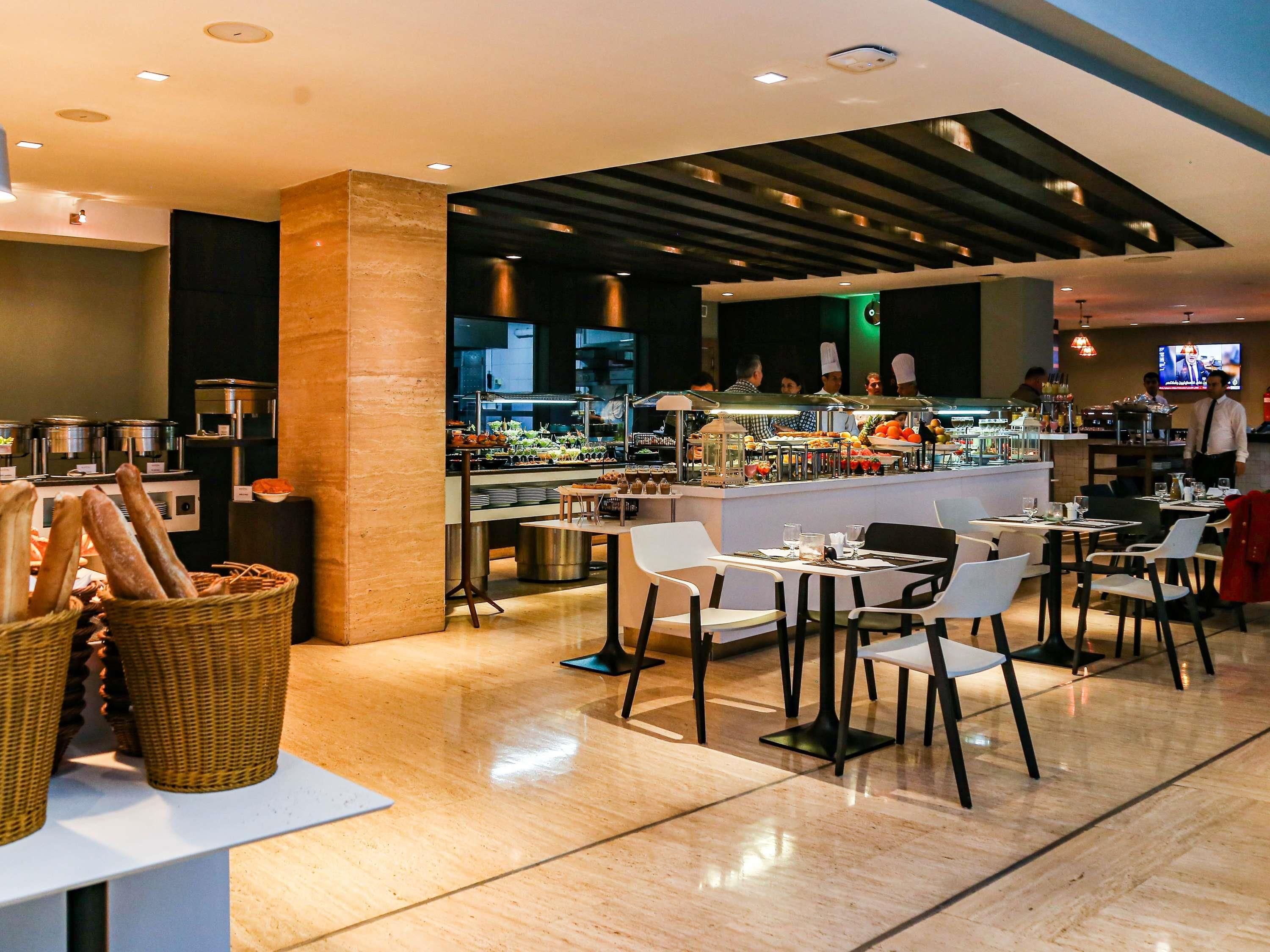 Un restaurante moderno con barra central, mesas para comensales y una cocina a la vista.