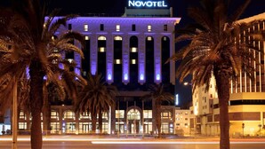 Un hotel con un llamativo letrero de 'NOVOTEL', que presenta una fachada moderna con detalles de iluminación vertical y una entrada simétrica.