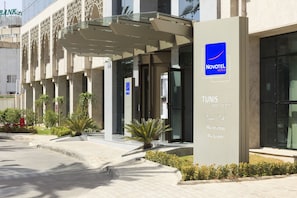 Entrada de un hotel Novotel con diseño moderno, que incluye un vestíbulo cubierto y una señalización.