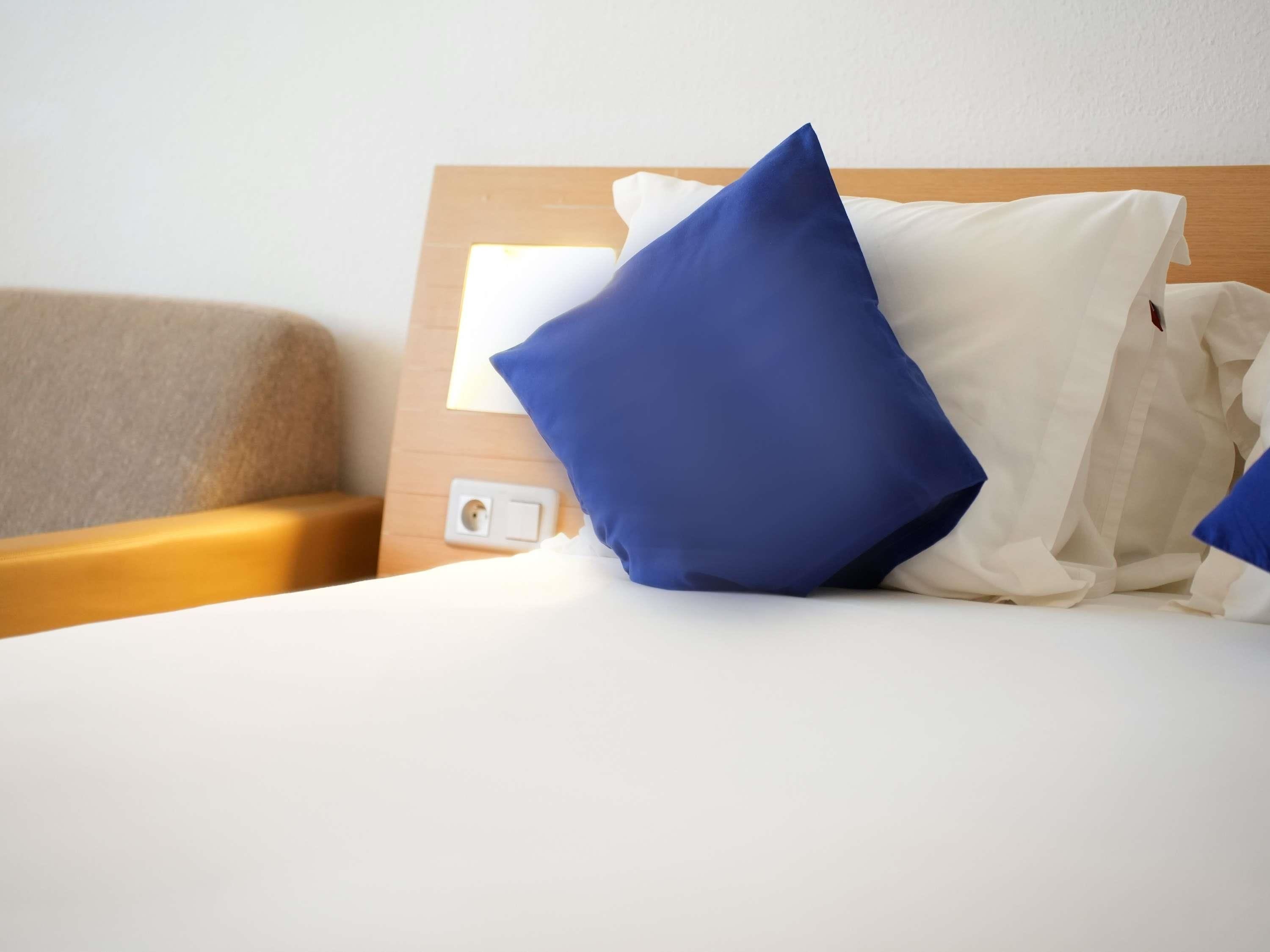 A hotel room with a bed, a wooden headboard, and a bedside table.