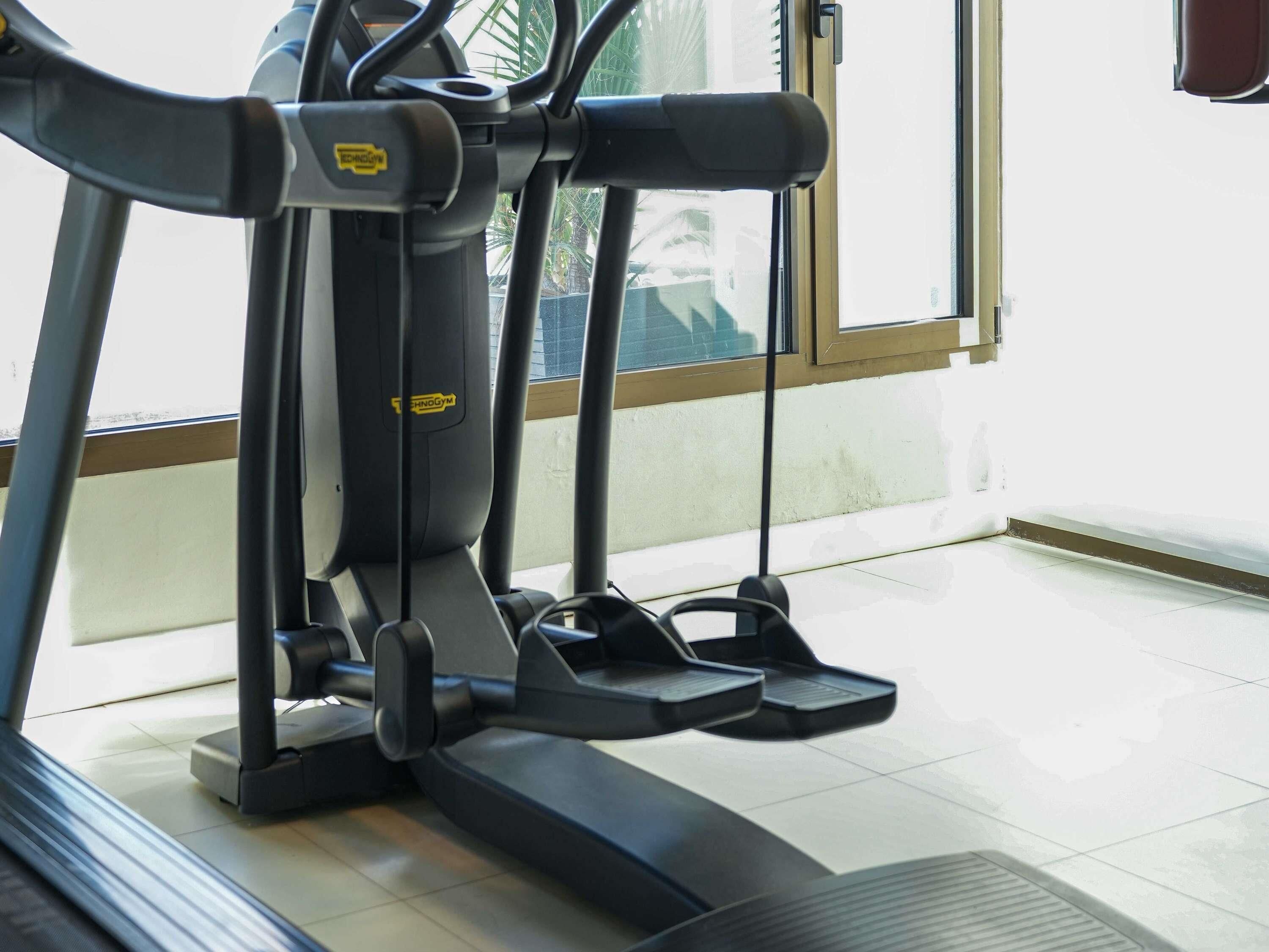 Un vélo d’appartement doté d’un écran numérique, d’un téléviseur fixé au mur et d’une fenêtre donnant sur des palmiers.
