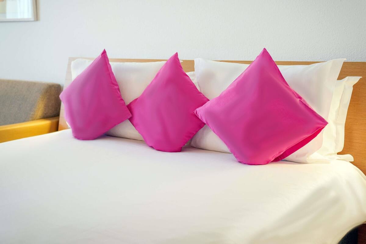 A bed with white bedding and three bright pink pillows.