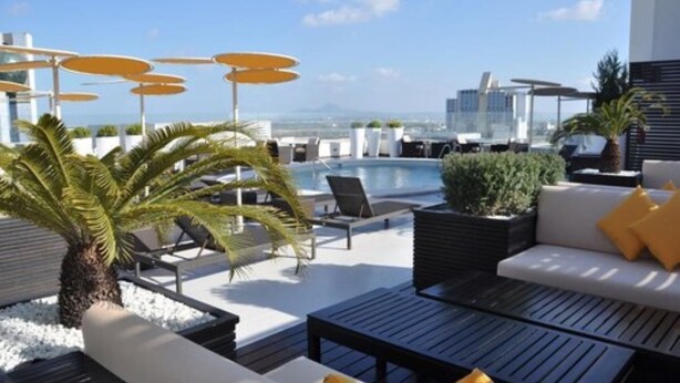 Un salón en la azotea con asientos al aire libre, piscina y vistas panorámicas de la ciudad.
