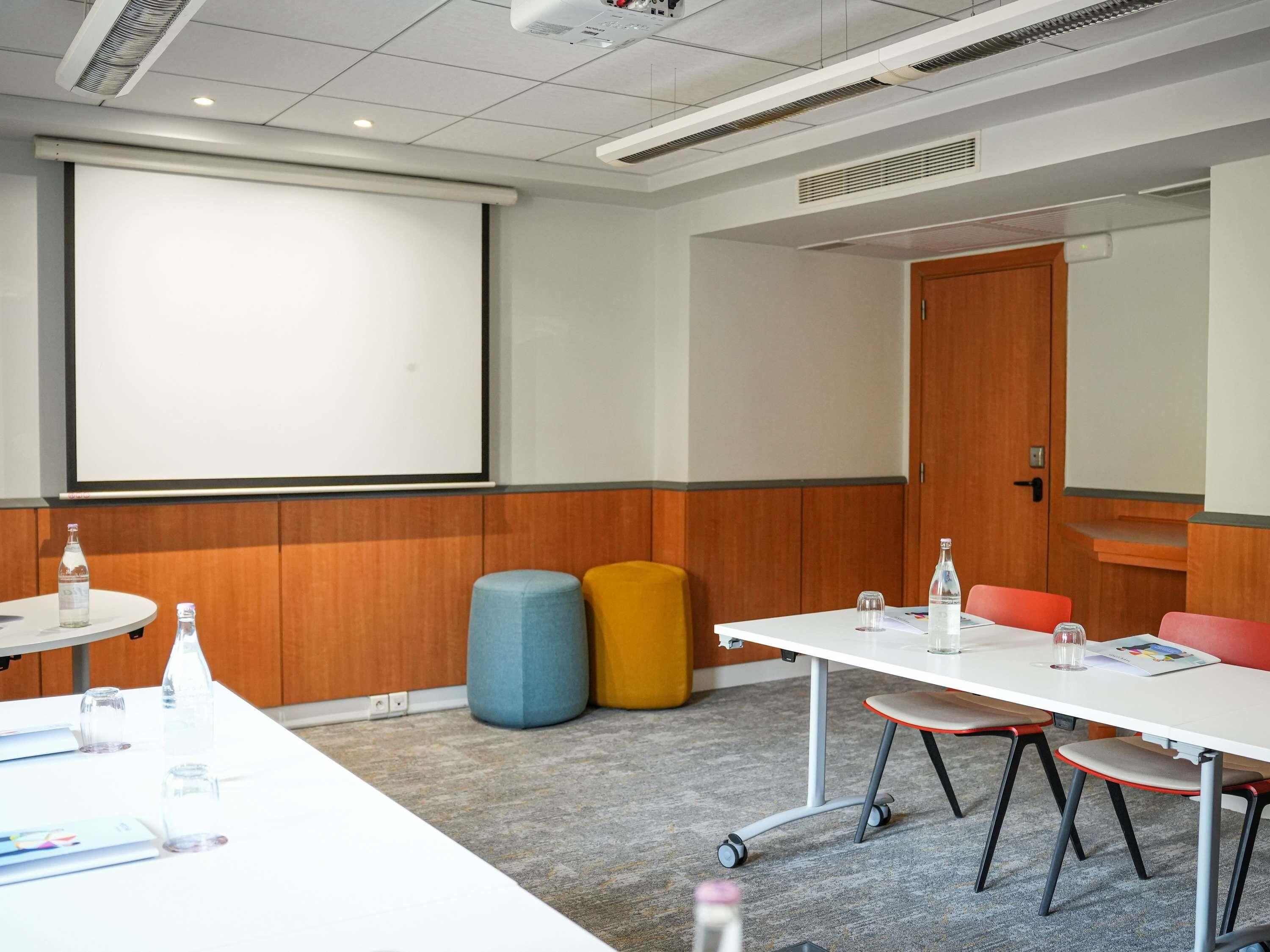 A conference room with a white table, chairs, a projector screen, and a wooden panel wall.
