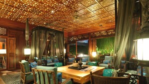 A traditional room with a wooden ceiling, green upholstered furniture, and a large window with a view of greenery outside.