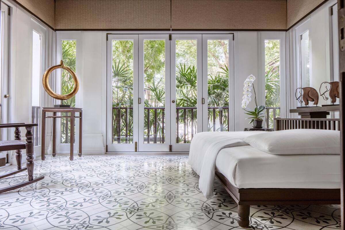 A bedroom with a bed, a round mirror, a small table, and a view of greenery through the glass doors.