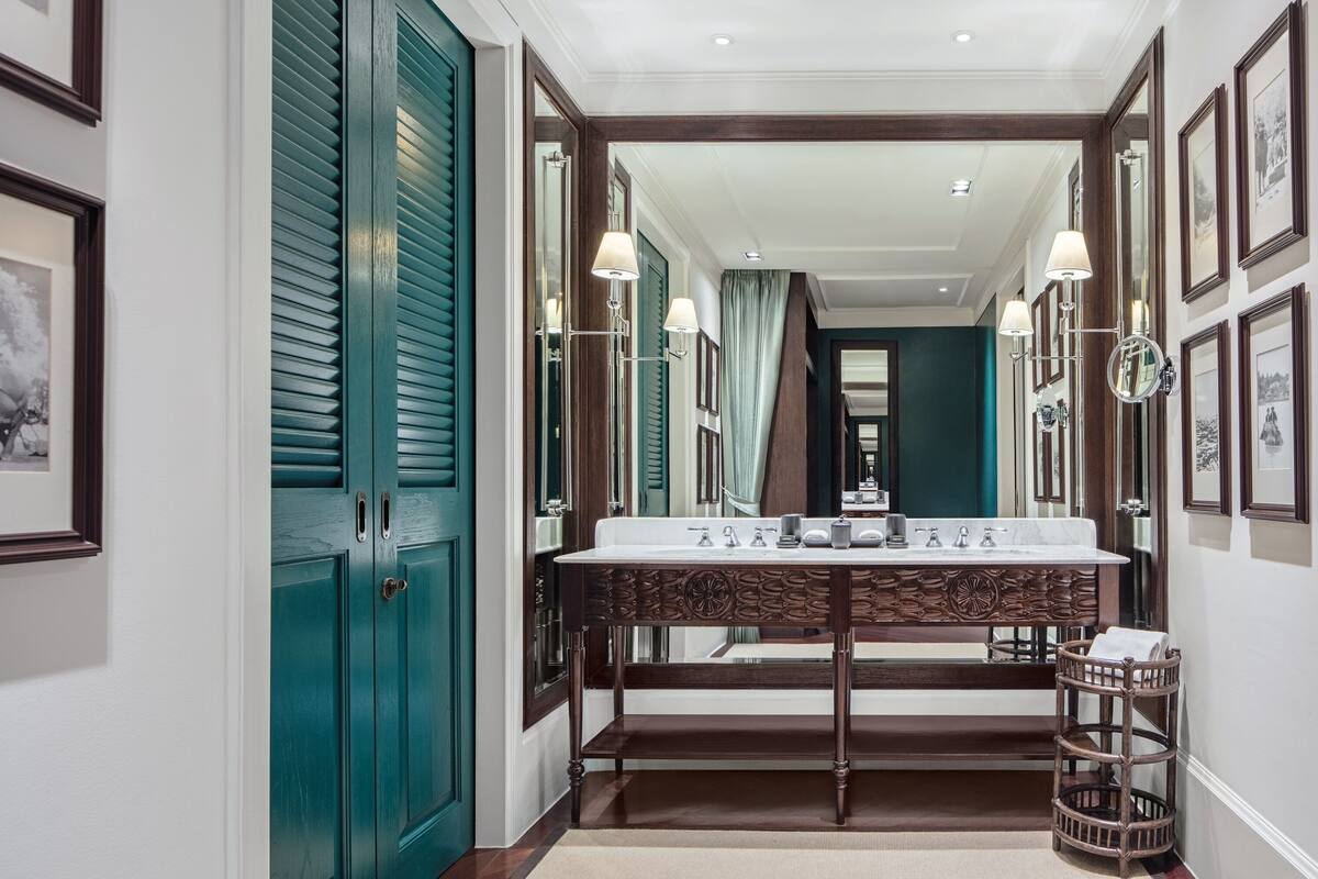 A hallway leading to a bathroom with a vanity, mirrors, and a wicker basket.